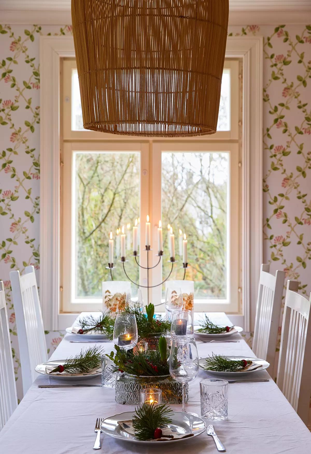 Праздничный стол с белой скатертью, подсвечником, бокалами, еловыми ветками в тарелках