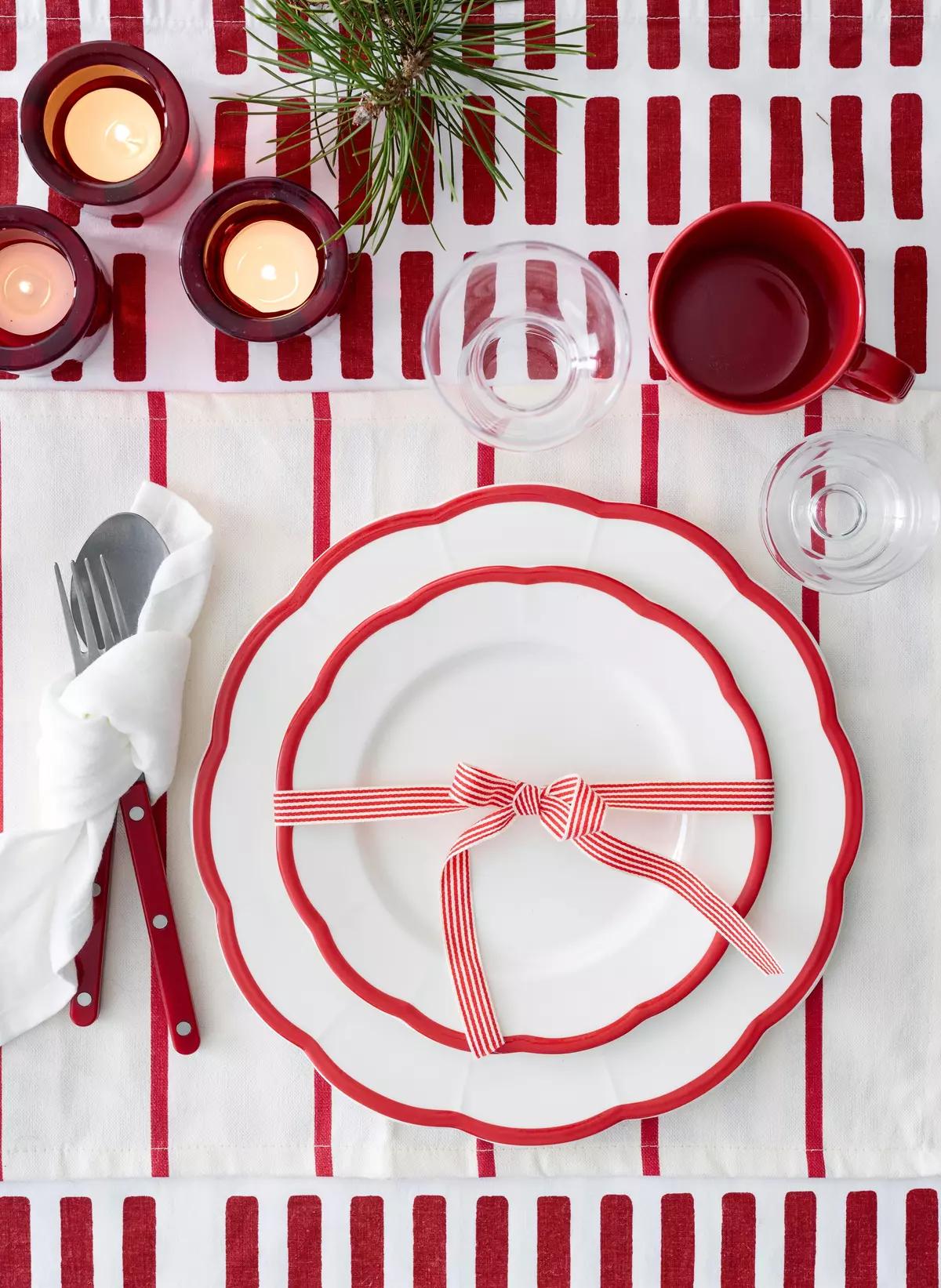 Новогодняя сервировка на красной полосатой скатерти с белой тарелкой, красной лентой