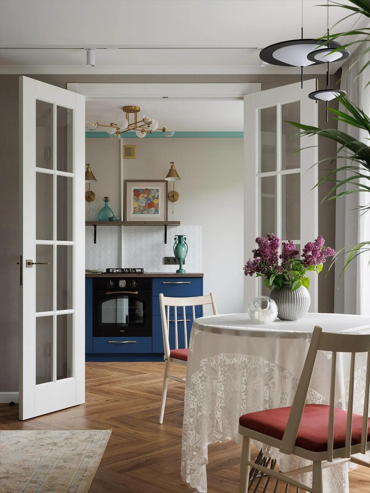 Круглый стол с белой скатертью на фоне кухни. На столе ваза с цветами