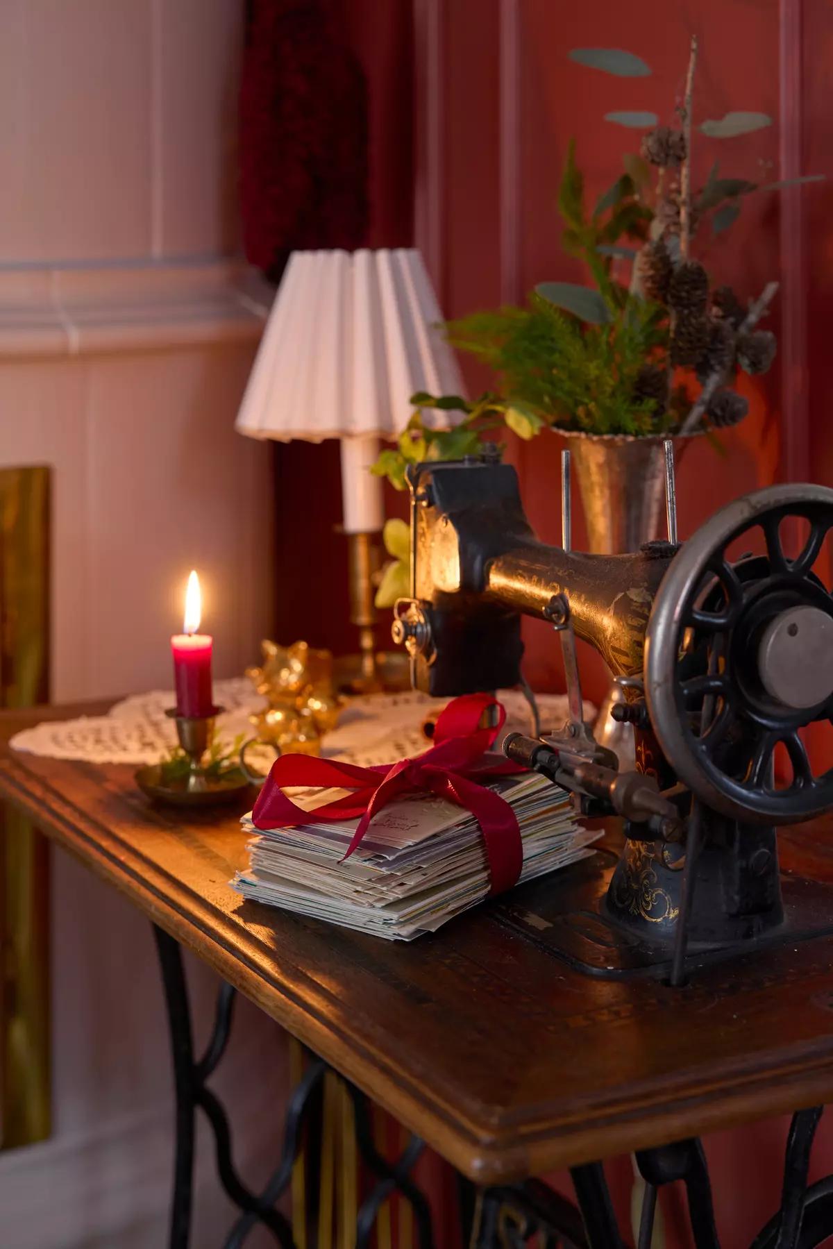 Швейная машинка, стопка открыток, перевязанных красной лентой и горящая свеча