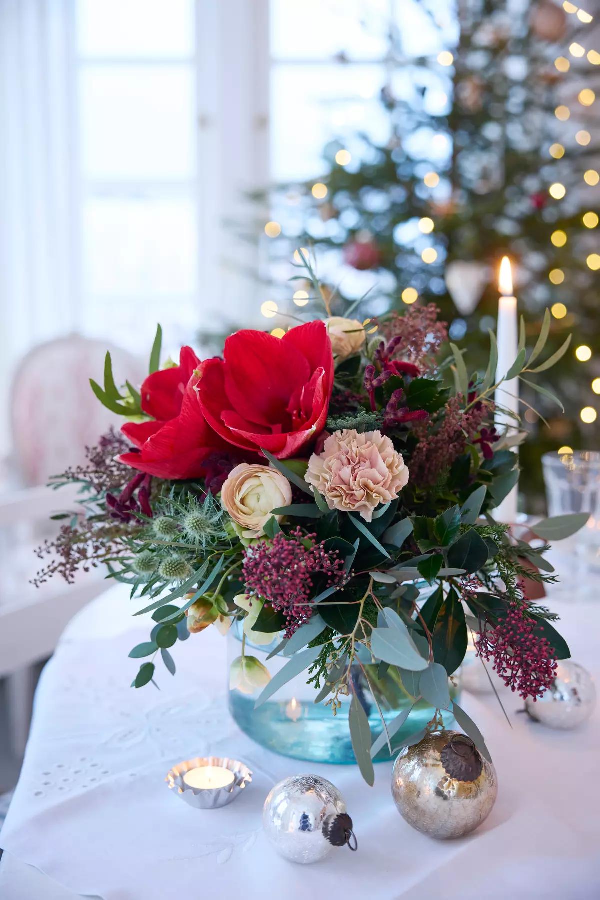 Праздничная цветочная композиция в бирюзовой вазе на фоне рождественской елки