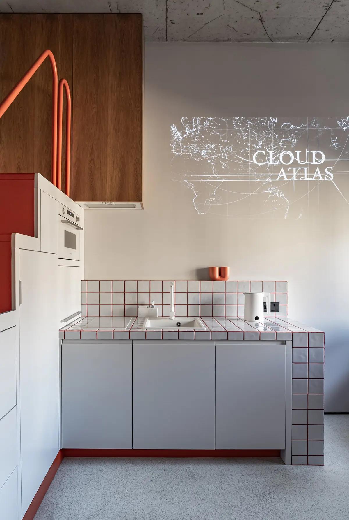 Кухонная зона с раковиной, белым электрическим чайником и проекцией фильма на стене, фартук с красными акцентами