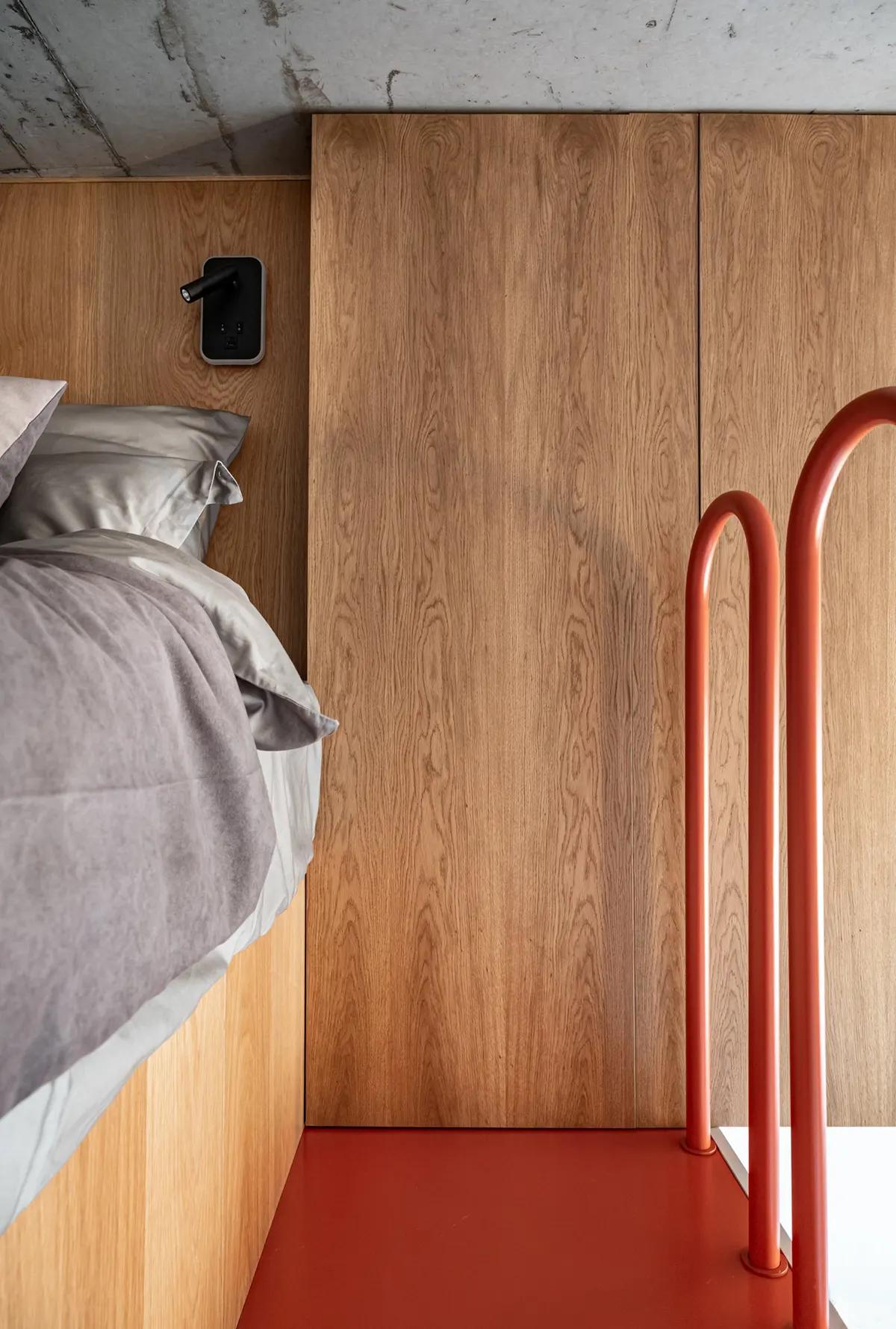 Спальня на антресоли с красной лестницей, деревянными панелями и серым постельным бельем