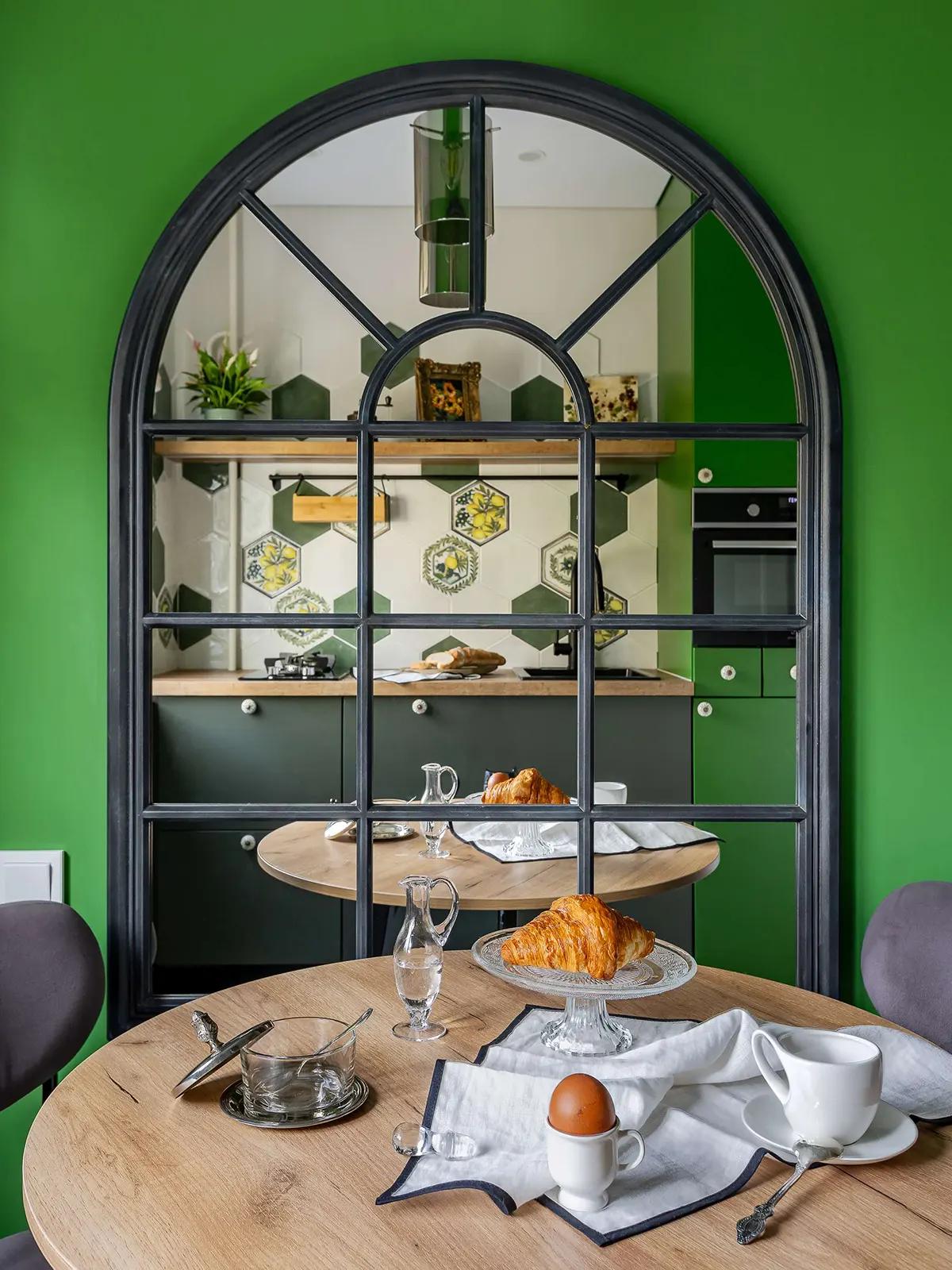 Арочное зеркало в черной раме на стене на кухне. Круглый стол с винтажной посудой