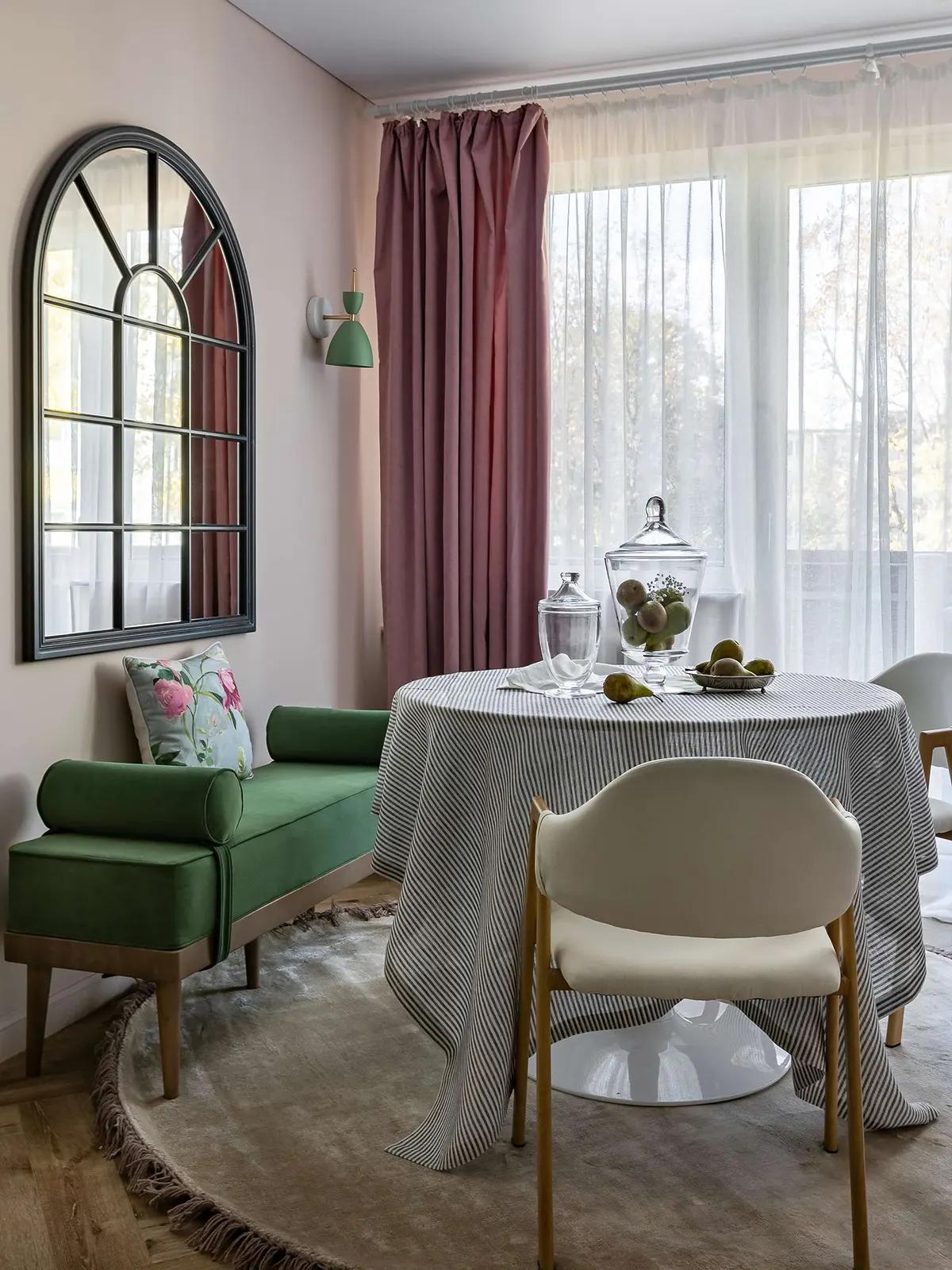 Обеденная зона с зеленой банкеткой, столом, полосатой скатертью, арочным зеркалом на стене и розовыми шторами в гостиной