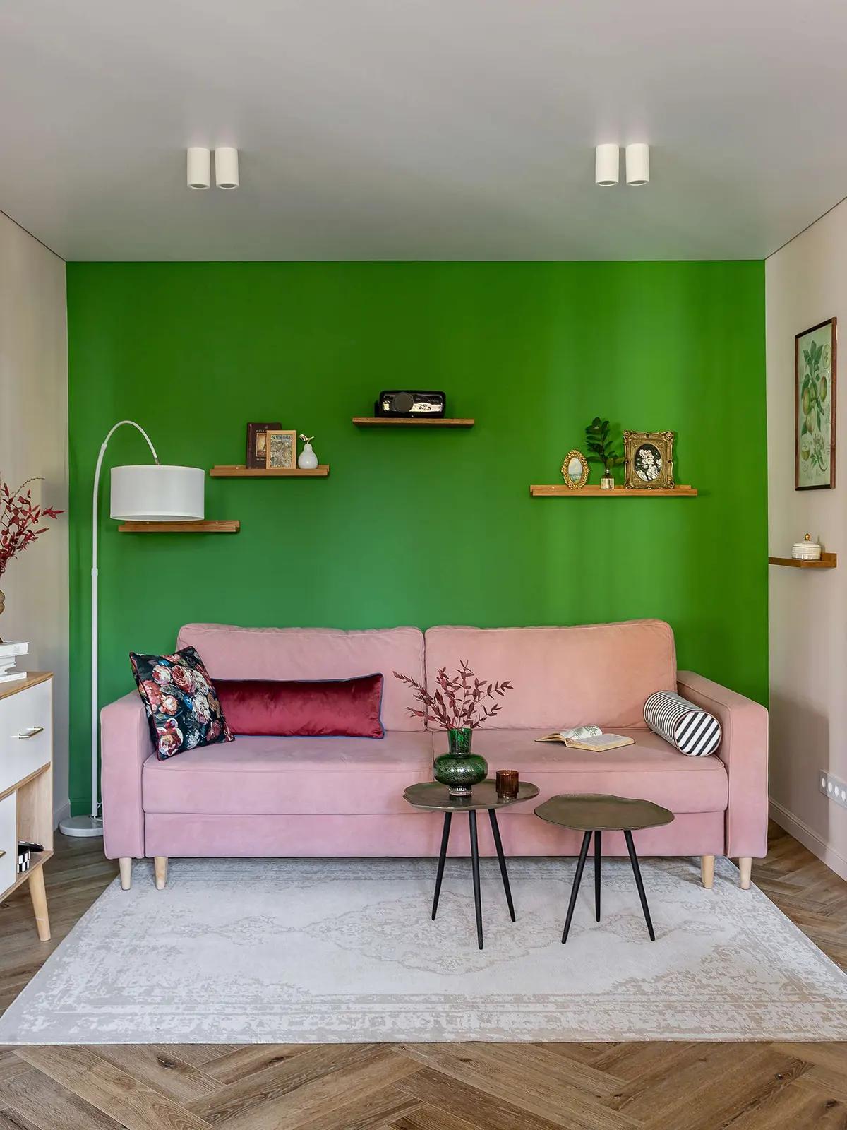 Ярко-зеленая акцентная стена в гостиной хрущевки, розовый диван с подушками, деревянные полки с декором на стене