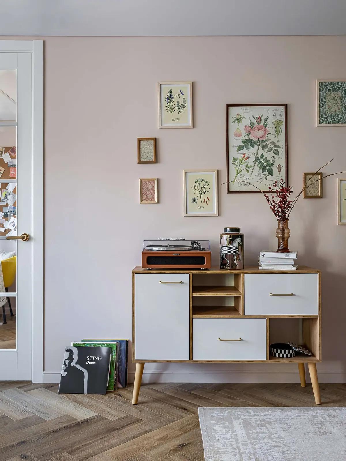 Ретро-комод у розовой стены, виниловый проигрыватель, стопки книг, ваза с ветками, ботанические принты, пластинки на полу