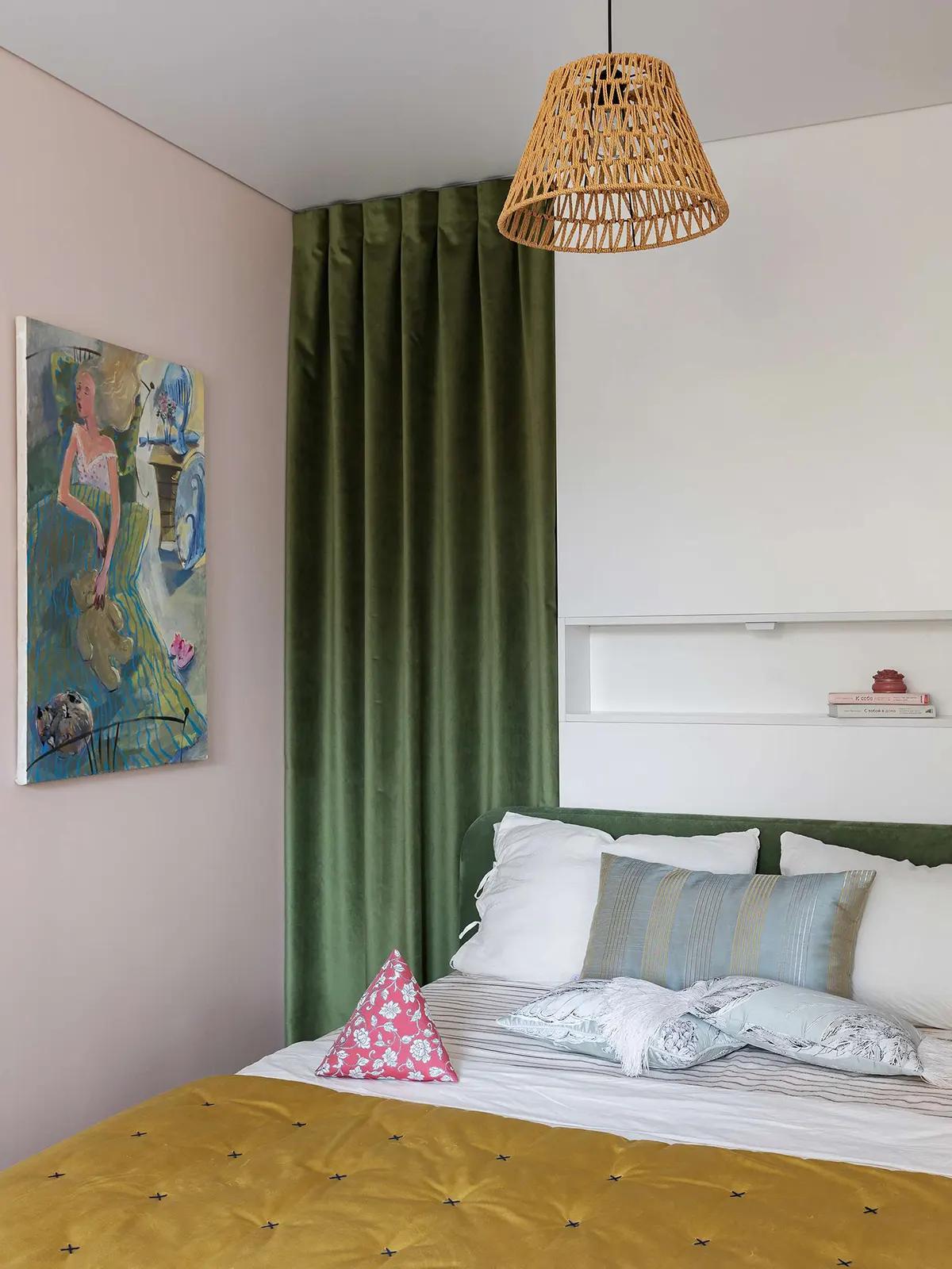 Спальня в хрущевке, зеленая бархатная штора, ротанговая лампа, абстрактная картина, зеленое изголовье с узорными подушками и горчичным одеялом