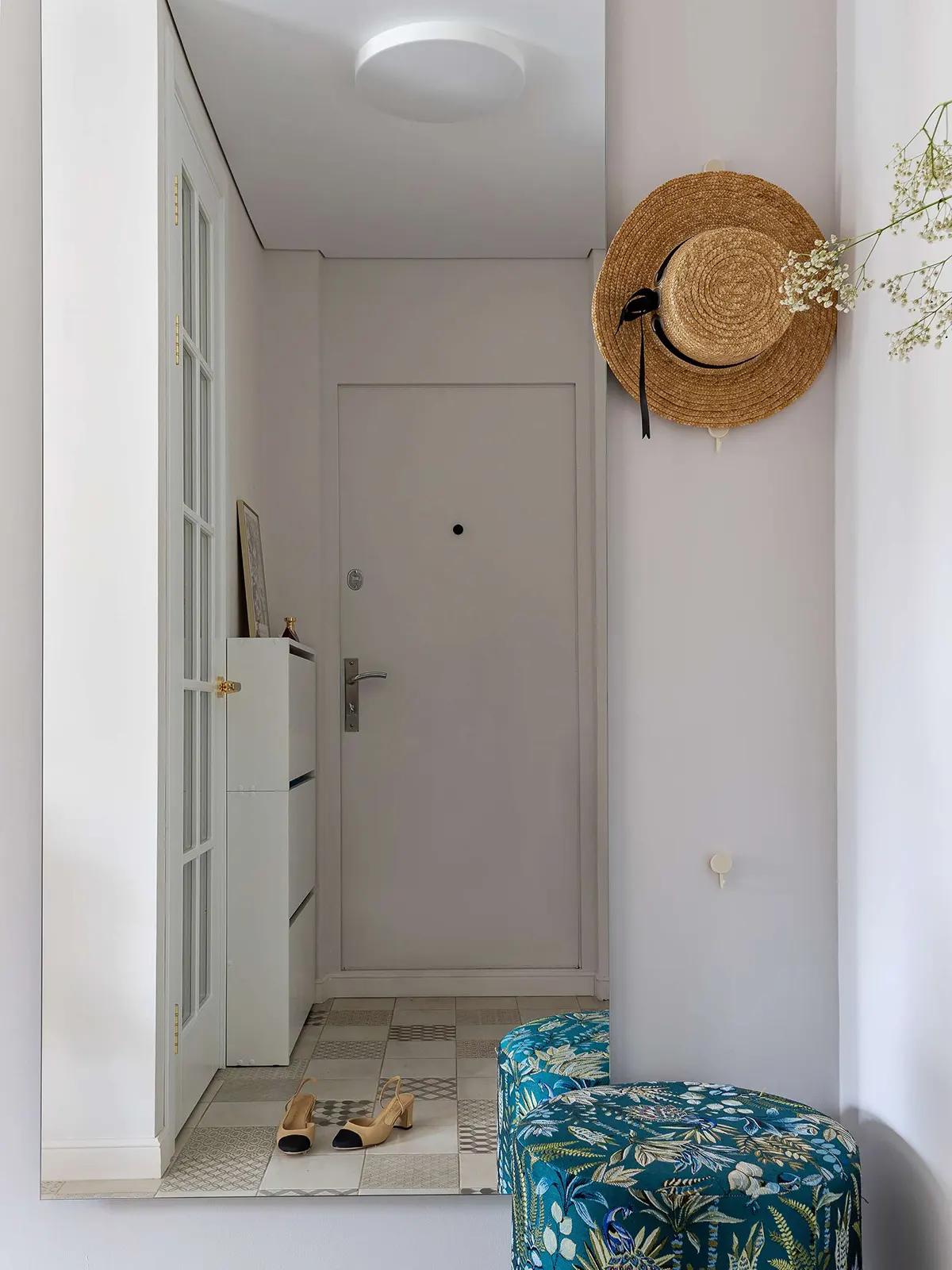 Прихожая в хрущевке с белыми стенами, узкими ящиками, соломенная шляпа на стене