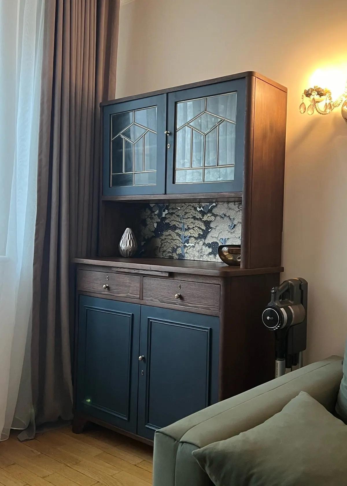 Реставрированный буфет в темно-синем оттенке с витражными стеклянными дверцами, деревянной столешницей и декоративным фоном из обоев