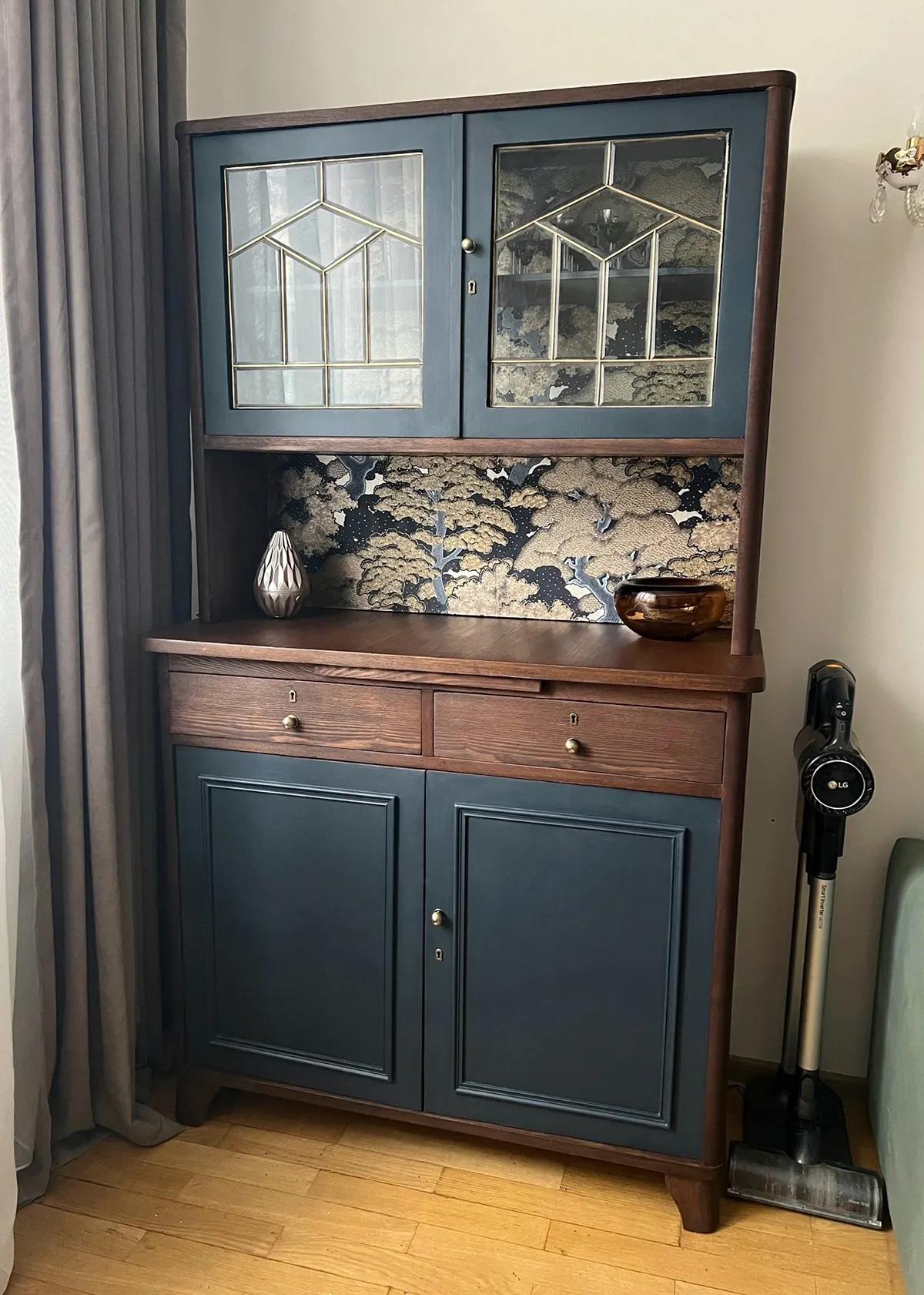Обновленный советский буфет в темно-синем исполнении со стеклянными дверцами, декоративной полкой и обоями в восточном стиле