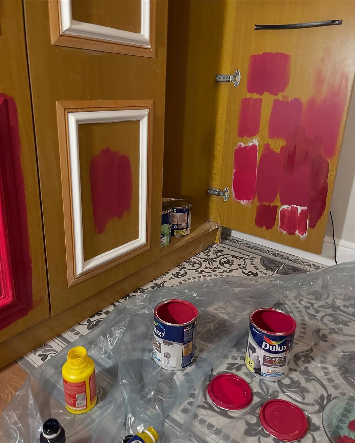 Тестирование оттенков красной краски на дверцах старого шкафа во время реставрации советской мебели, с банками Dulux на полу