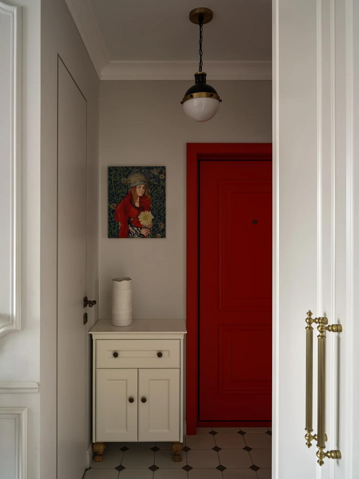 Прихожая с красной входной дверью, белым шкафчиком и картиной на серой стене