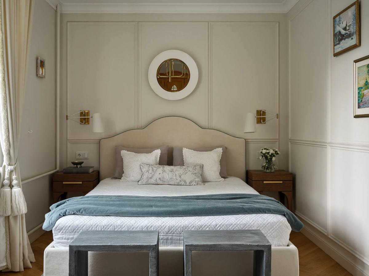 Светлая спальня в пастельных тонах, круглым белым зеркалом, картинами пейзажей