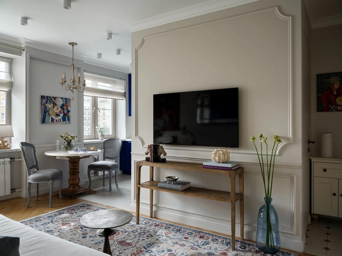 Гостиная с телевизором на стене, деревянным массивным столом и стульями в обеденной зоне у окна