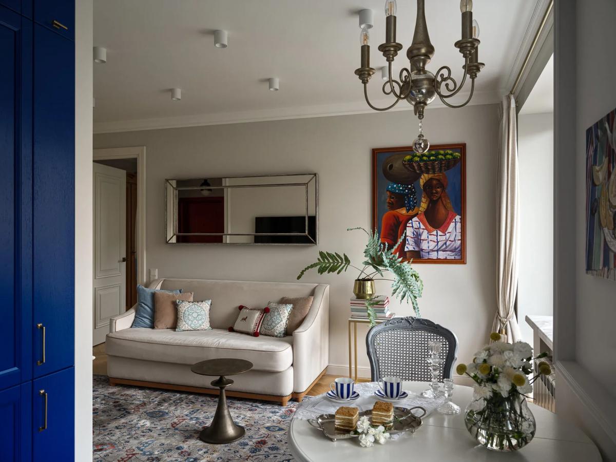 Гостиная с белым диваном, зеркалом и африканской картиной на стене, цветами в вазе и чайным сервизом на столе