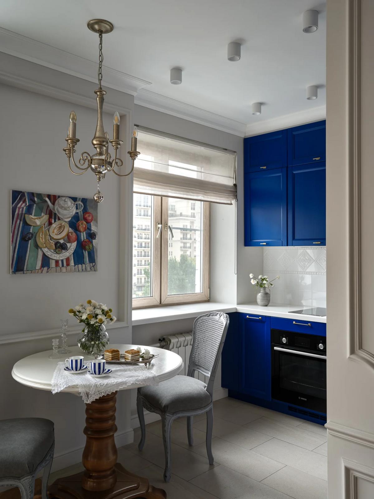Кухня в хрущевке с синими шкафами, натюрмортом с фруктами, круглым столом и чаем у окна